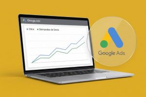 Ordinateur portable posé sur fond jaune affichant un tableau de bord Google Ads avec deux courbes ascendantes, l'une pour les clics et l'autre pour les demandes de devis.